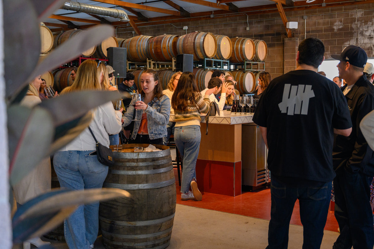 Guests talking around a wine-barrel table and the bar at Muni Ventura.